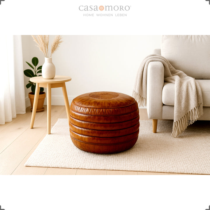 Lys stue i skandinavisk stil med en rund læderpuf i brun på et tæppe, en beige sofa og en træskammel med en vase - en rolig, naturlig atmosfære.