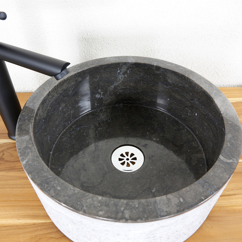 Detaljeret billede af en rund håndvask i sten med en mørk inderside, præcist udformet og et klart formsprog.