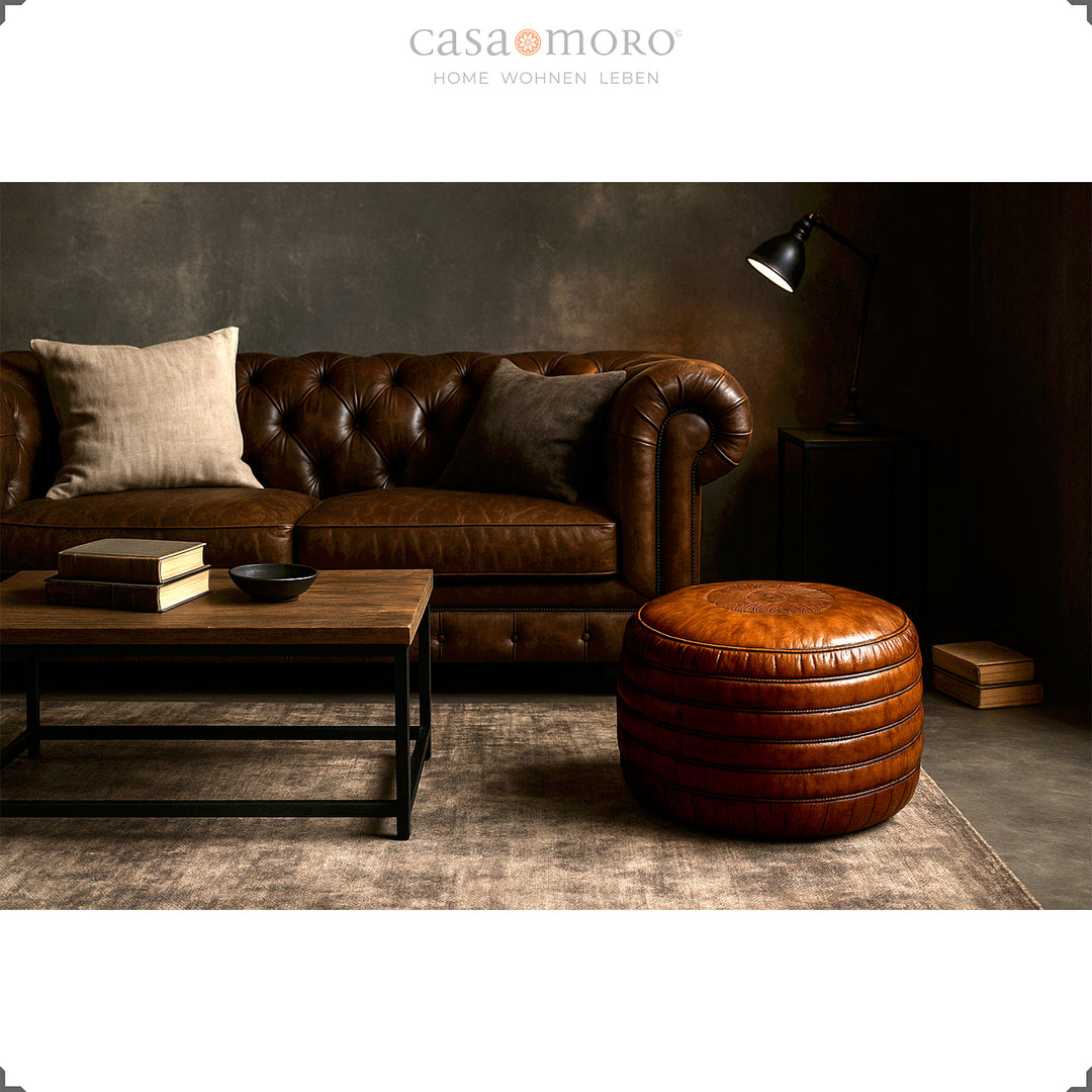 Elegant stue med Chesterfield sofa, sofabord og rund læderpuf i brun - stilfuld scene i industriel og moderne-rustik stil.