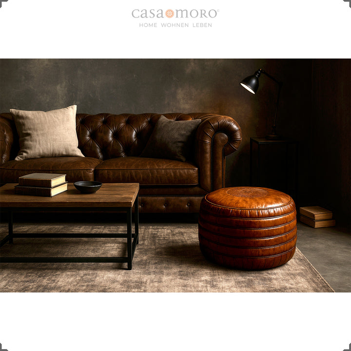 Elegant stue med Chesterfield sofa, sofabord og rund læderpuf i brun - stilfuld scene i industriel og moderne-rustik stil.