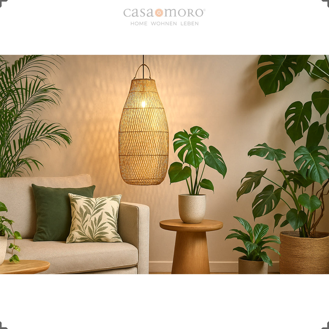 Stor rattan loftslampe over sofa i stue med masser af grønne planter og varmt lys