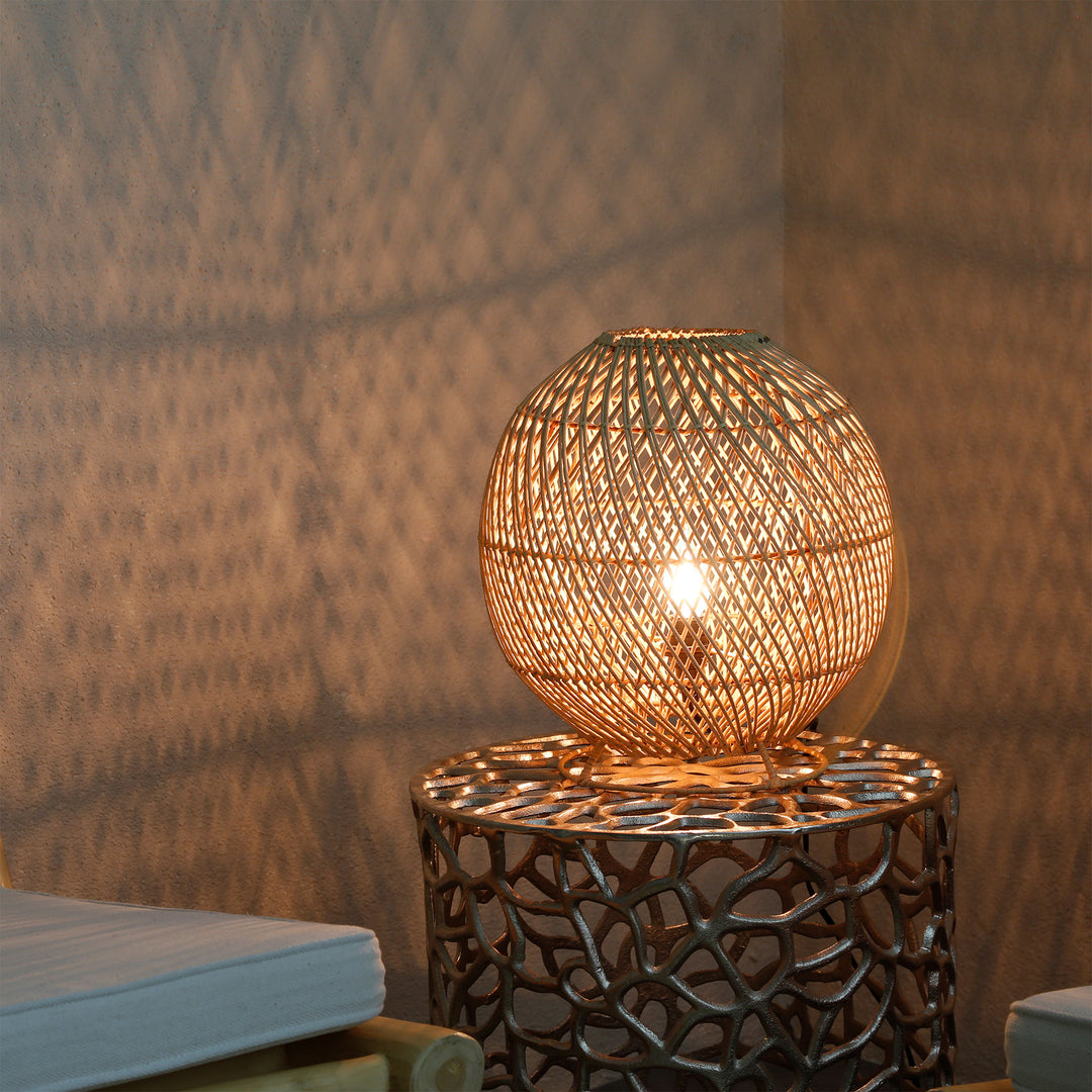 Rund rattanlampe på et sidebord i stuen med et fint lysmønster på væggen