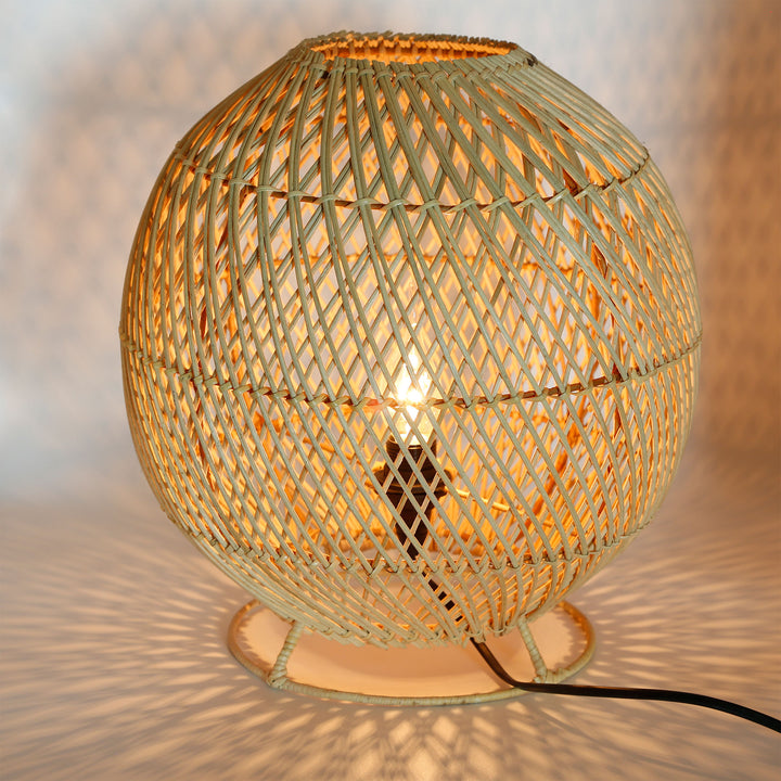 Rund gulvlampe i rattan med fint vævet mønster og varmt lysspil på væg og gulv