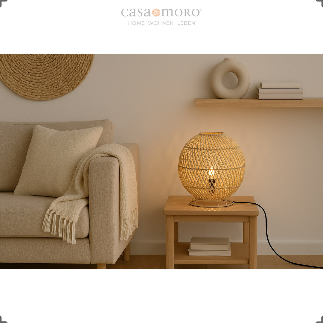 Rund rattan bordlampe på sidebord ved siden af sofa, varmt lys og naturlig indretning