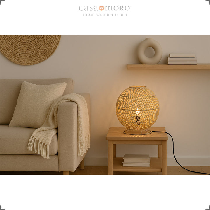 Rund rattan bordlampe på sidebord ved siden af sofa, varmt lys og naturlig indretning
