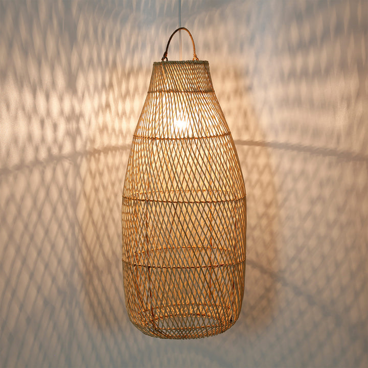 Høj rattanlampe med fint vævningsmønster og et varmt lysspil på væggen