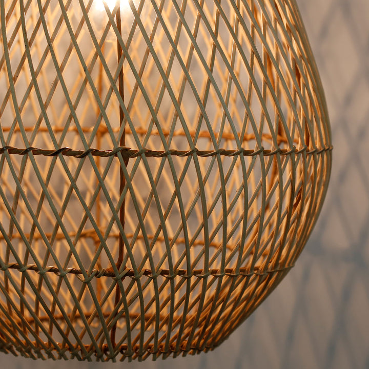 Detaljeret billede af en håndlavet rattanlampe med et fint, diagonalt vævningsmønster og varmt lys